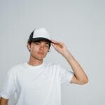 Portrait of a young man in a white shirt and a cap posing in a studio setting.